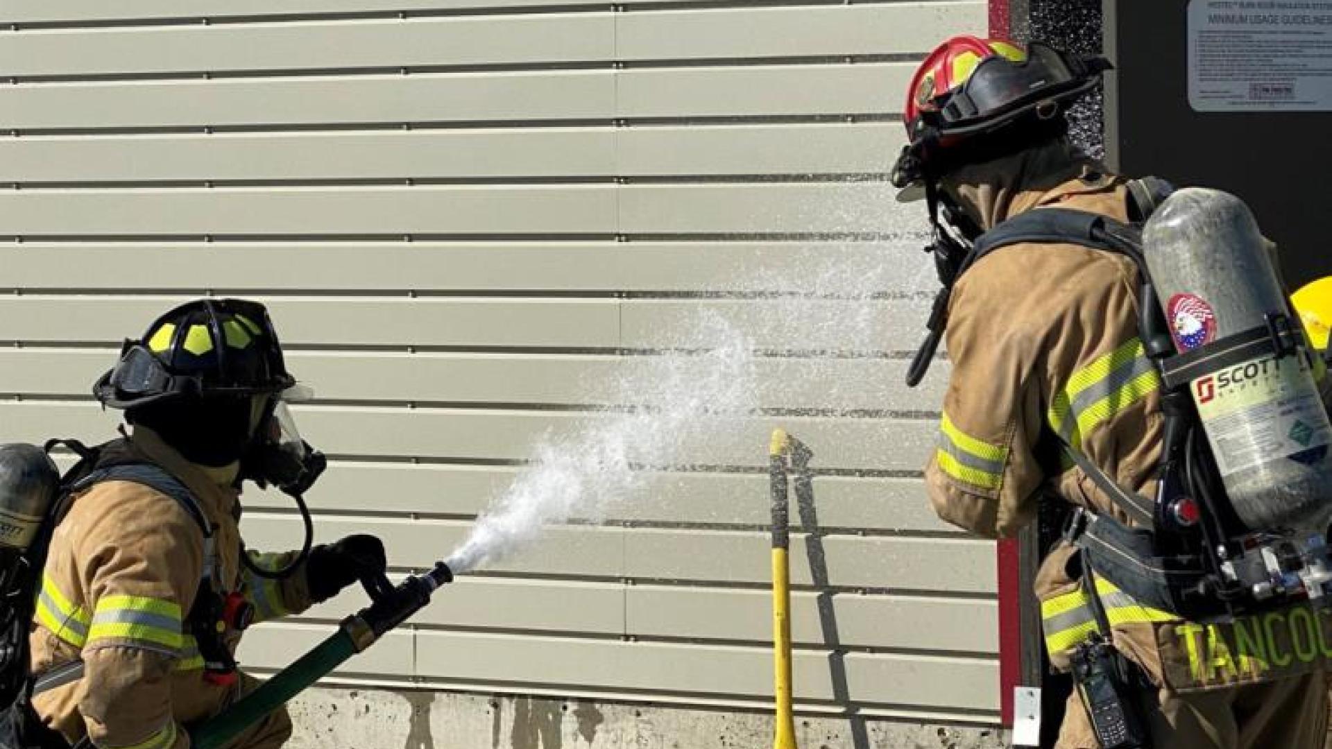 Two firefighters practice fire suppression from the exterior.
