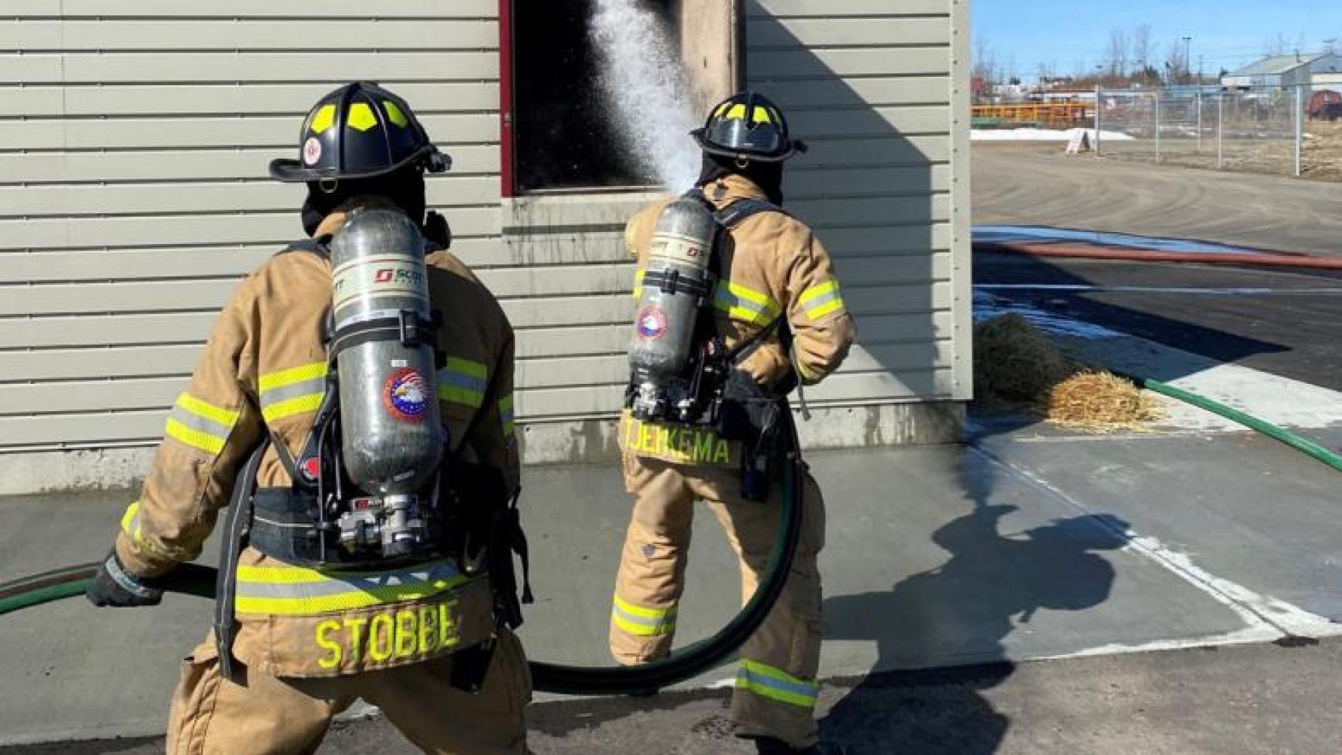 Two firefighters practice fire suppression from the exterior.