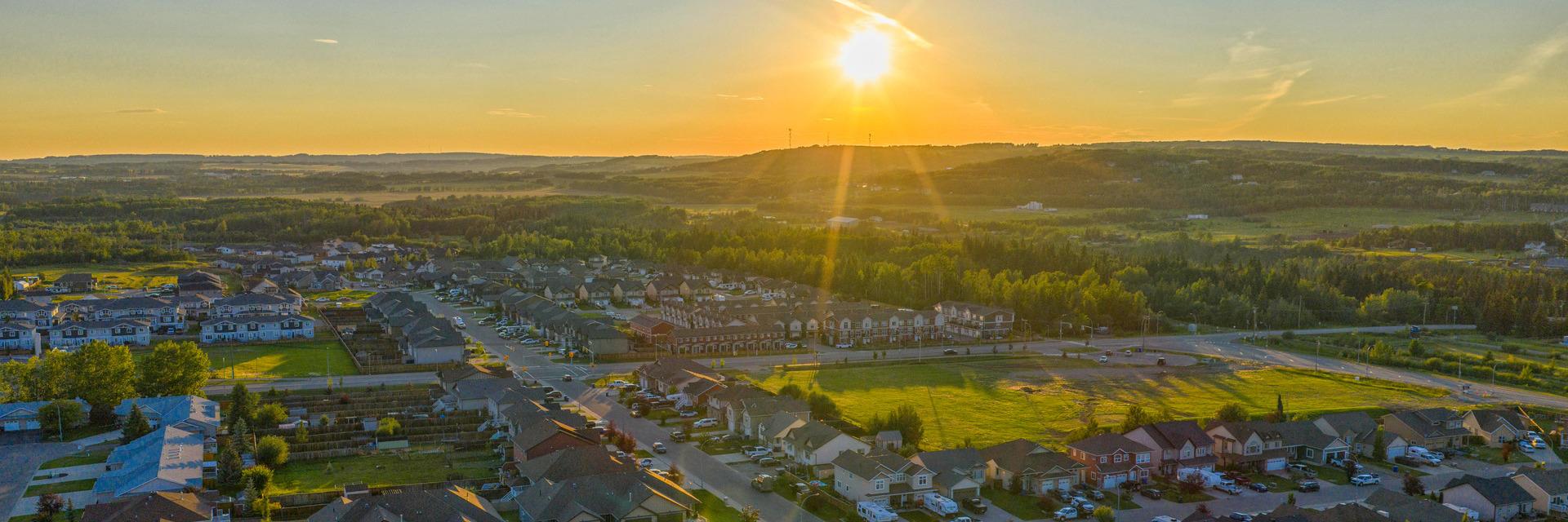 Aerial view of the City at golden sunset, with homes, green fields, and wooded hills.