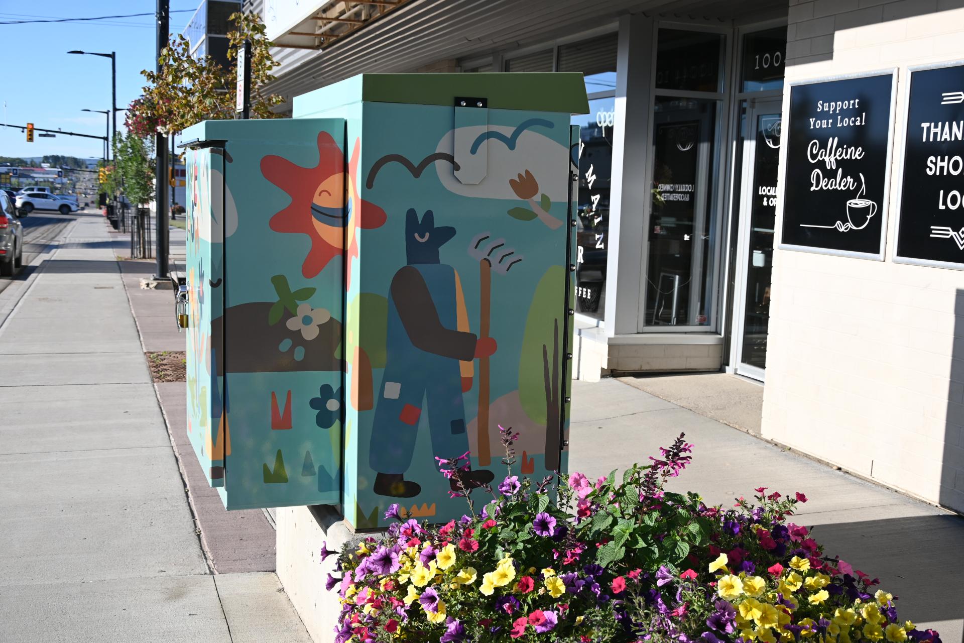 A colorful utility box mural with abstract nature design, featuring a smiling sun, person with rake, and flowers